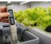 Hand holding an EC meter showing a high reading over a hydroponic nutrient reservoir